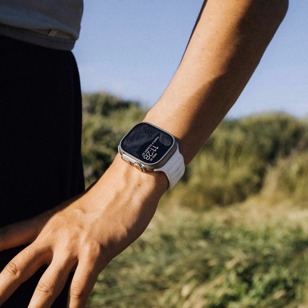 Смарт-часы Apple Watch Ultra с белым перфорированным ремешком на фоне ландшафта, надежное крепление и комфортная посадка на руке