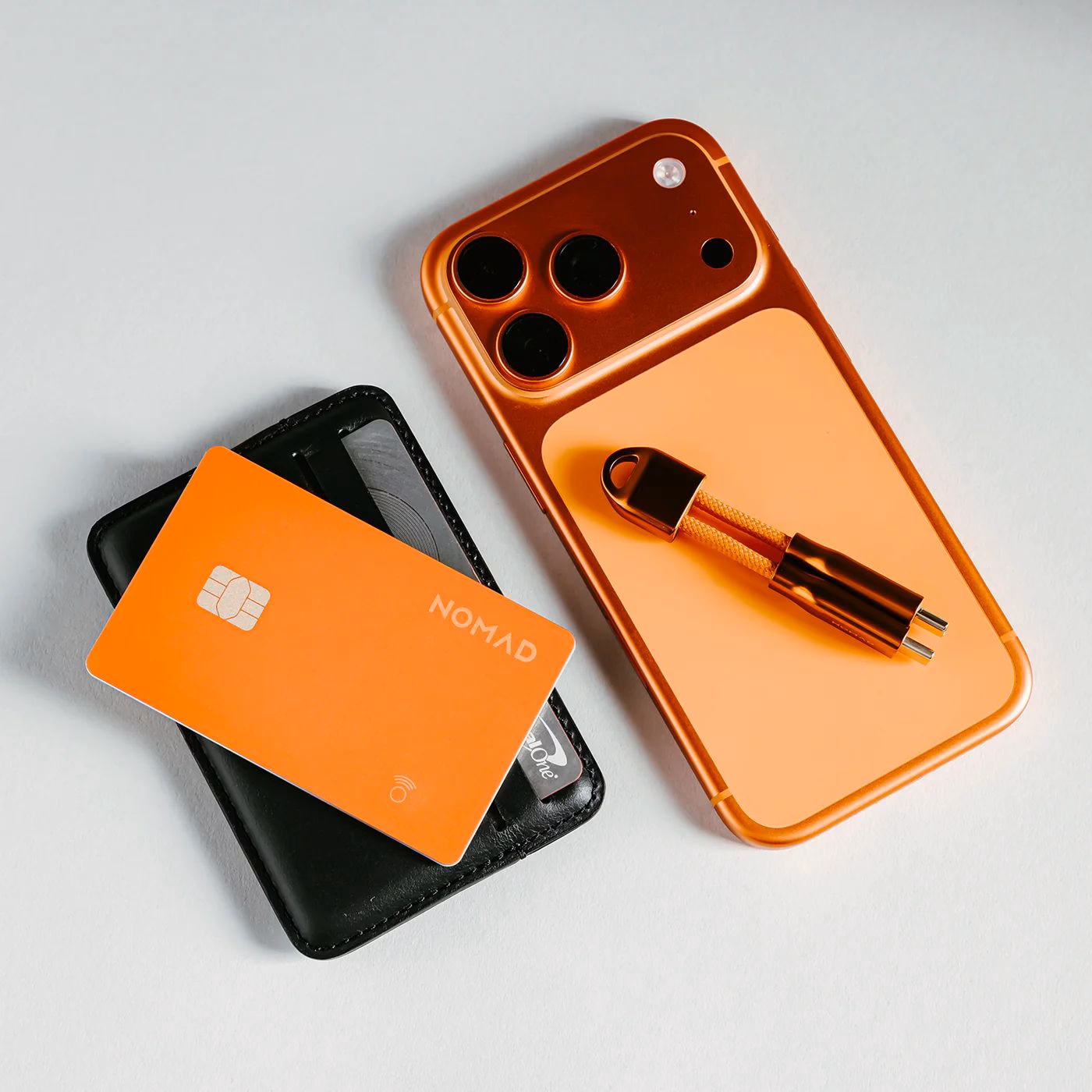 Трекер Nomad Pro Stellar Orange поруч з iPhone та аксесуарами
