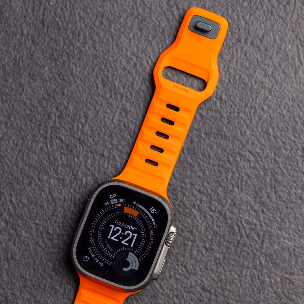 Apple Watch Ultra з встановленим яскраво-помаранчевим ремінцем Nomad Sport Band на темно-сірому фоні, деталізація текстури FKM.